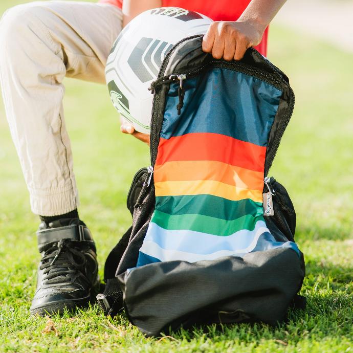 A person placing a soccer ball into a retro stripe eco friendly chicobag travel pack rePETe lightweight back pack made from recycled materials